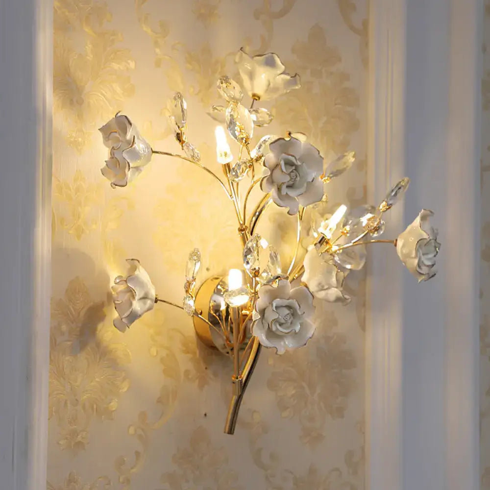 Elegant gold-toned wall lamp with white porcelain roses and crystal accents for contemporary bedroom light fixture