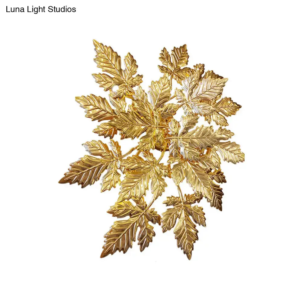 Contemporary gold finish wall mount sconce featuring a golden metallic brooch with detailed maple leaf design