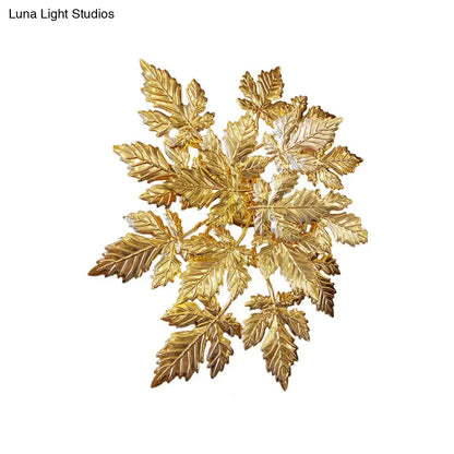 Contemporary gold finish wall mount sconce featuring a golden metallic brooch with detailed maple leaf design