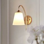 Contemporary gold milk glass wall lamp with frosted shade and curved metal arm as a bedroom sconce