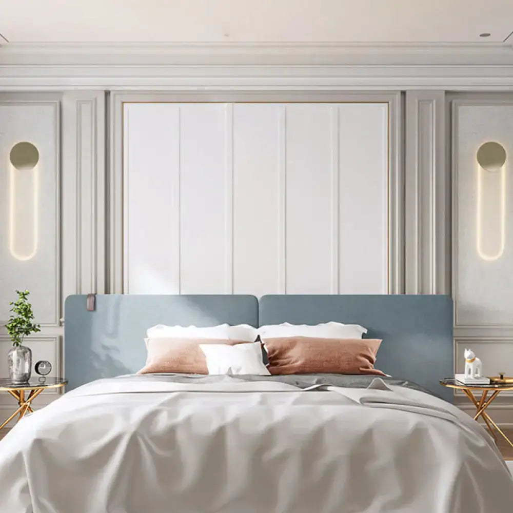 Contemporary gold oblong wall light fixture 110v 120v mounted above blue upholstered bed with white and rose gold pillows