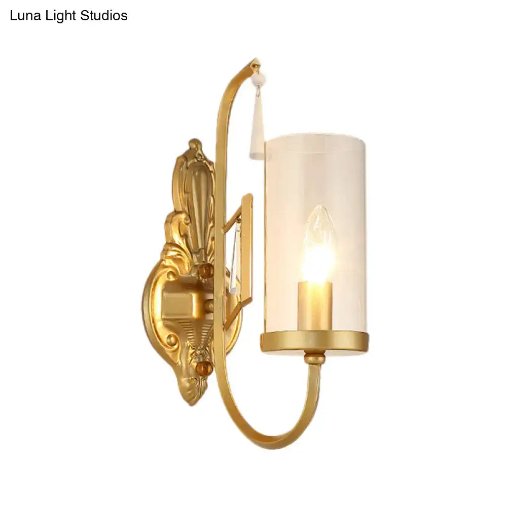 Contemporary gold wall light with an ornate design and cylindrical clear glass shade for bedroom use