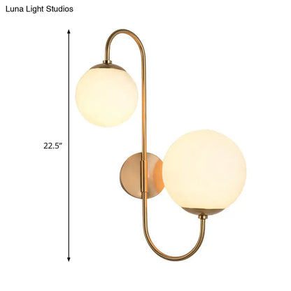 Contemporary gold wall sconce with brass finish and two spherical opal glass shade globes for bedroom lighting
