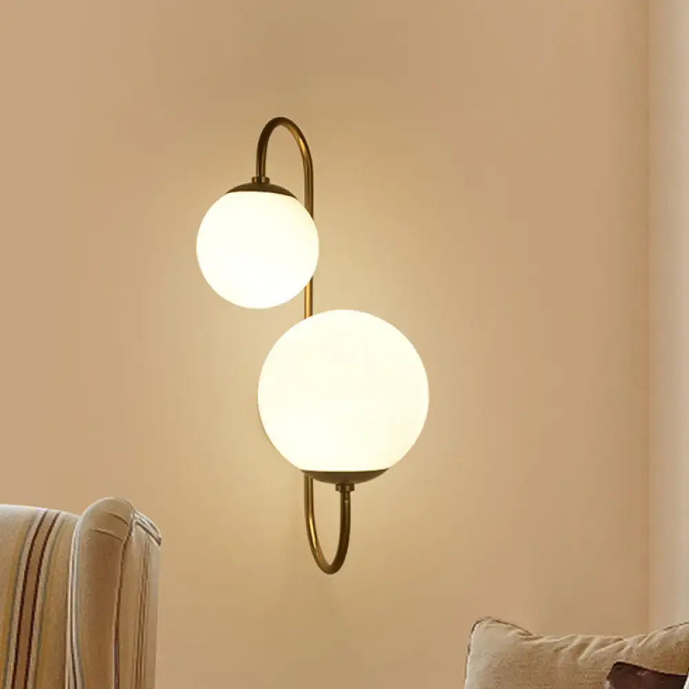 Brass-finished contemporary gold wall sconce with two frosted opal glass shade globes for bedroom lighting