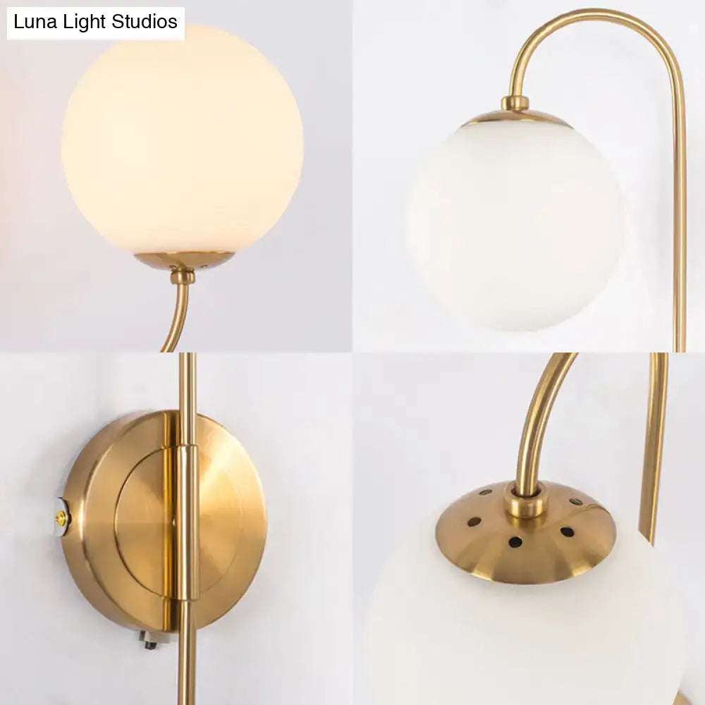 Contemporary gold wall sconce light with frosted opal glass globe and curved brass arm for bedroom lighting