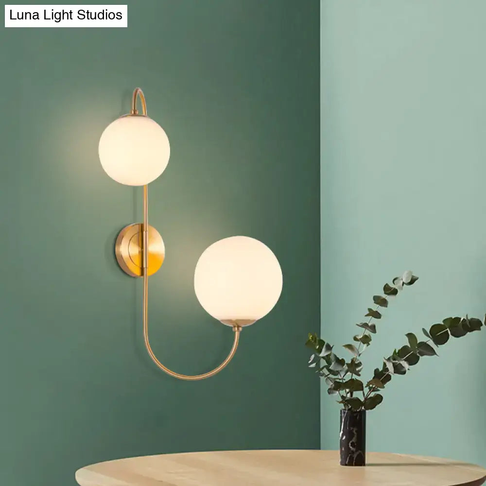 Contemporary gold wall sconce light with brass finish and two spherical frosted opal glass shades for bedroom use