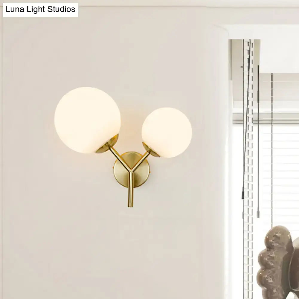 Contemporary gold-toned light fixture bedroom sconce with two frosted glass globe shades and shade width details