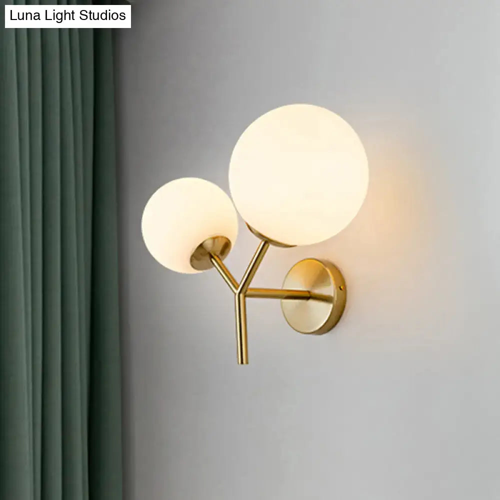 Contemporary gold light fixture with frosted white spherical glass shades and adjustable shade width for bedroom sconce