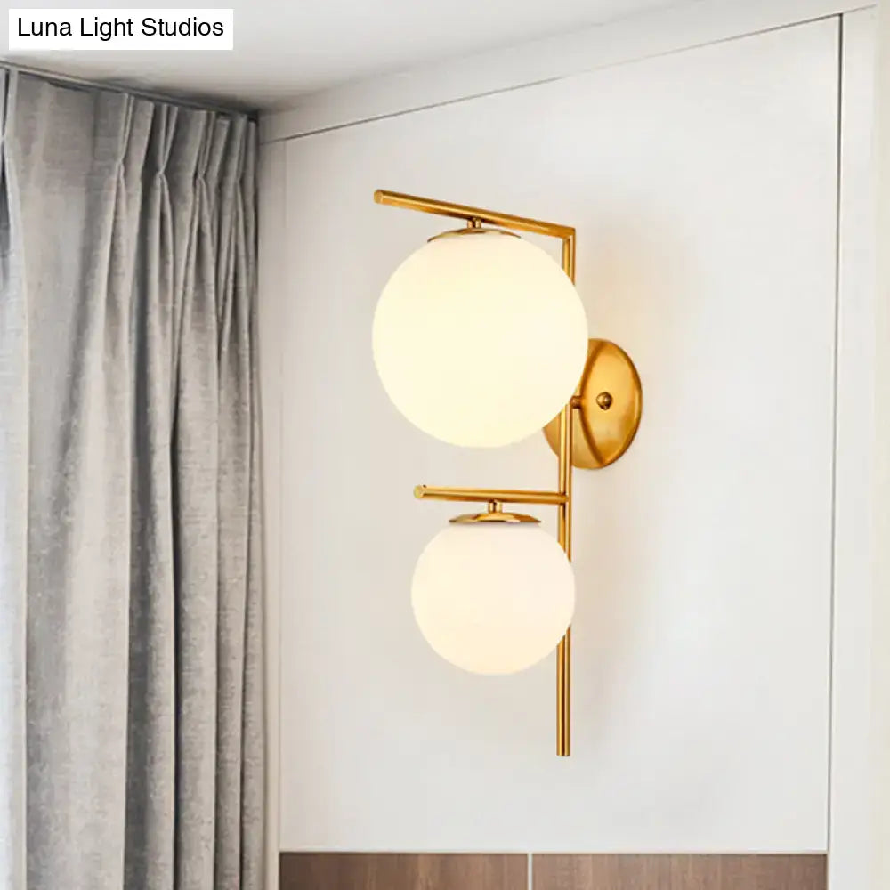 Contemporary gold light fixture with two frosted white spherical glass shades and moderate shade width bedroom sconce