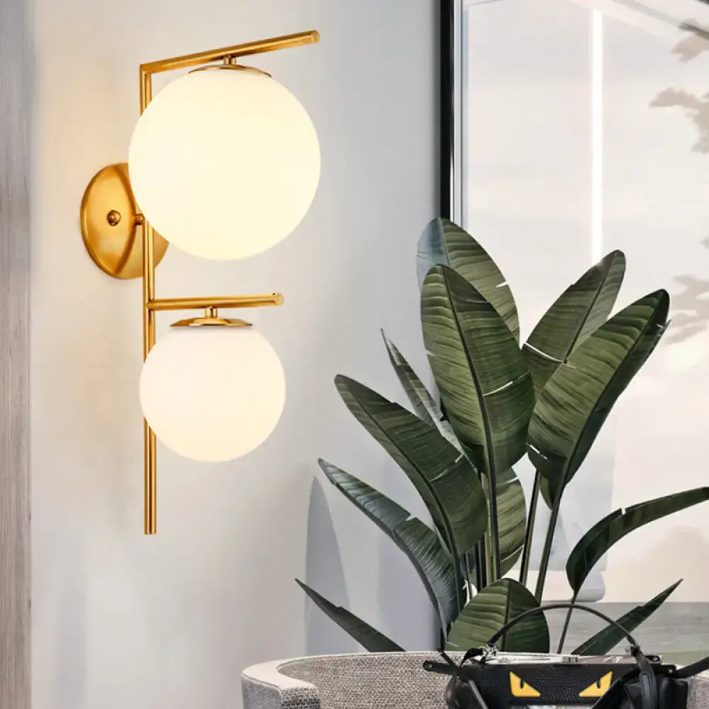 Contemporary gold light fixture with two spherical frosted glass shades and adjustable shade width for bedroom sconce