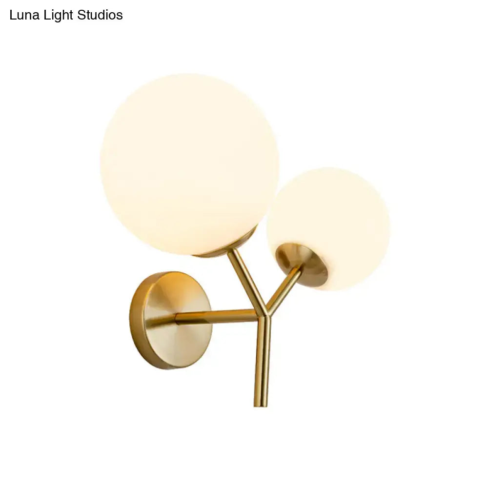 Contemporary gold light fixture with two frosted white glass globe shades and medium shade width bedroom sconce