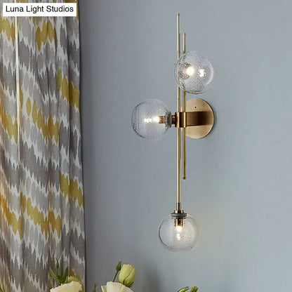 Contemporary brass wall sconce with three green clear glass globe shades and direct wired electric for living room use