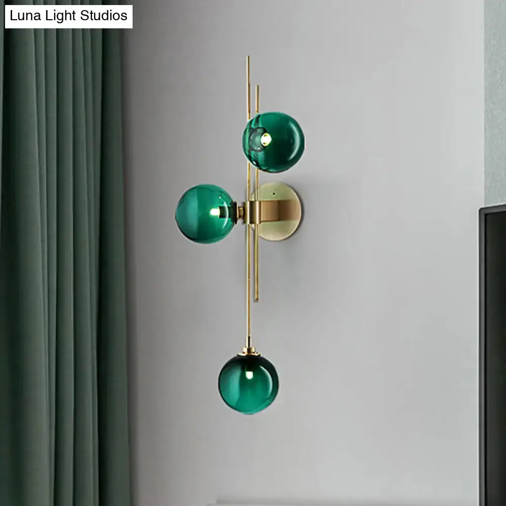 Contemporary living room wall sconce with three emerald green clear glass globes on brass direct wired electric frame