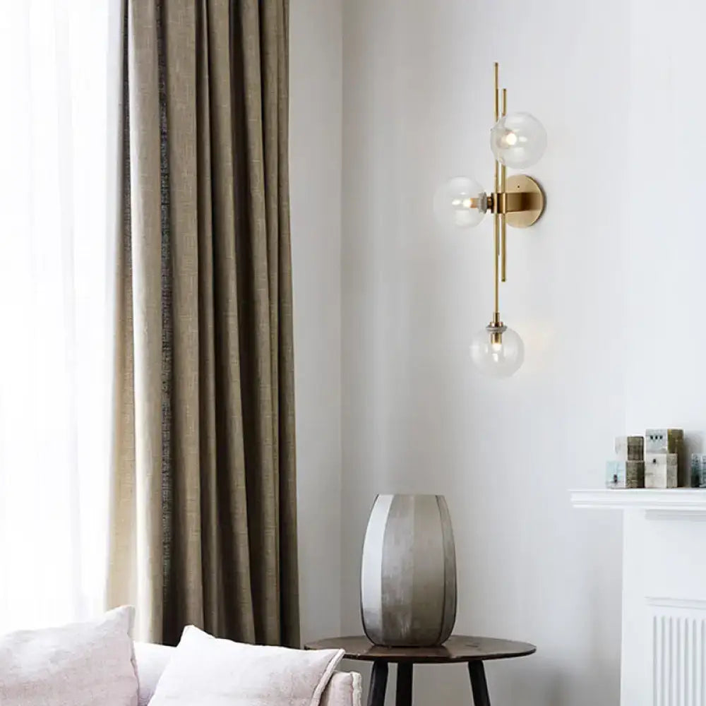 Contemporary gold-toned living room wall sconce with three vertically arranged clear glass globe bulbs and direct wired electric design