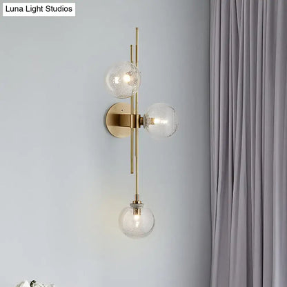 Contemporary brass-finished wall sconce with three clear glass globe shades arranged vertically for direct wired electric use