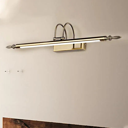 A sleek brushed brass wall-mounted vanity light with warm light and ornate curved finials for bedroom use