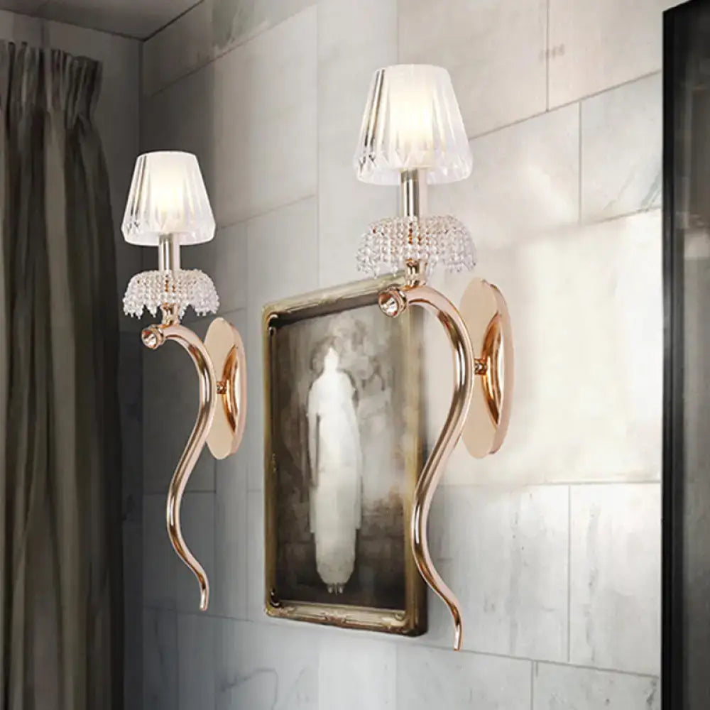 Contemporary rose gold wall sconce with gold-toned arms crystal embellishments and clear ribbed glass shade for bedroom lighting