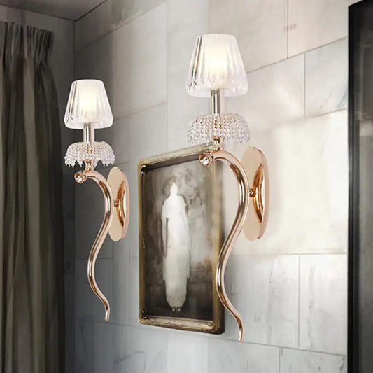 Contemporary rose gold wall sconce with gold-toned arms crystal embellishments and clear ribbed glass shade for bedroom lighting