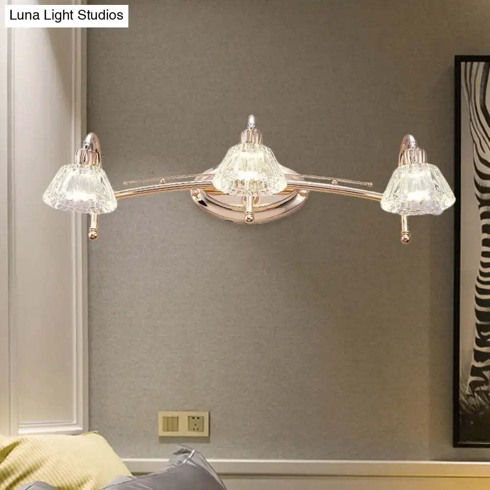 A sleek contemporary rose gold wall vanity light with three truncated cone faceted crystal shades