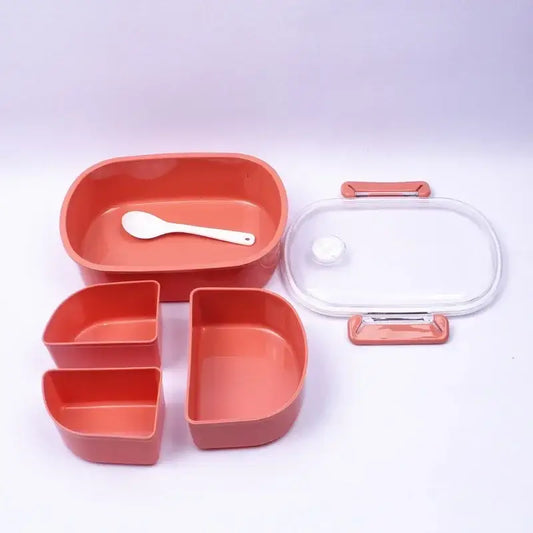 Coral-colored plastic lunch box set with three compartments, clear glass lid, and white spoon for kitchen use