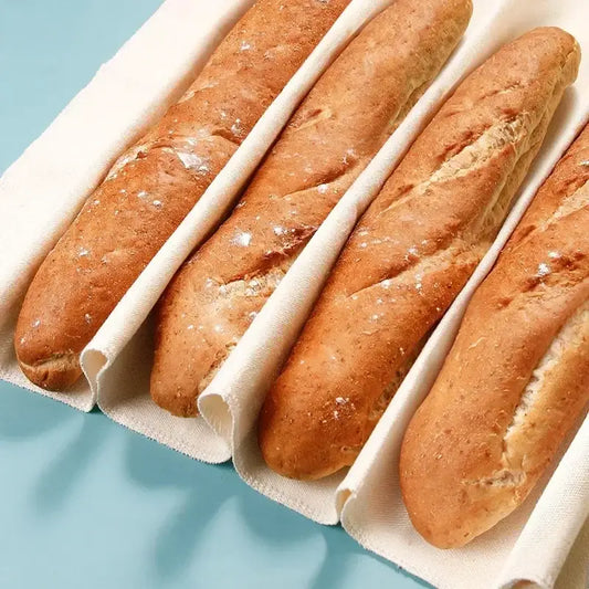 Four golden-brown baguettes in individual white cotton sleeves using a cotton baguette proofing cloth for baking