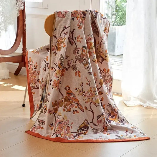 A cream-colored decorbites cotton gauze bath towel with orange bird and floral pattern and orange border for bedroom throw