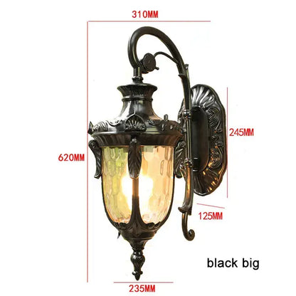 Black ornate wrought iron outdoor wall lantern with textured amber glass shade for country restaurant lighting