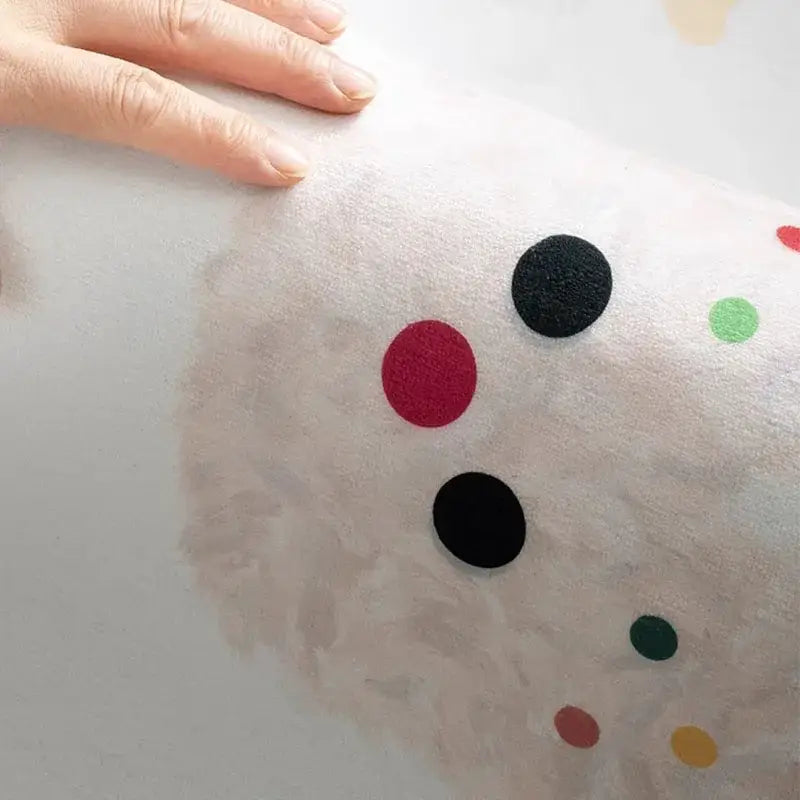 A soft off-white plush toy with colorful felt cartoon ball print polka dots displayed on a cozy carpet white and blue daisy embroidered rug