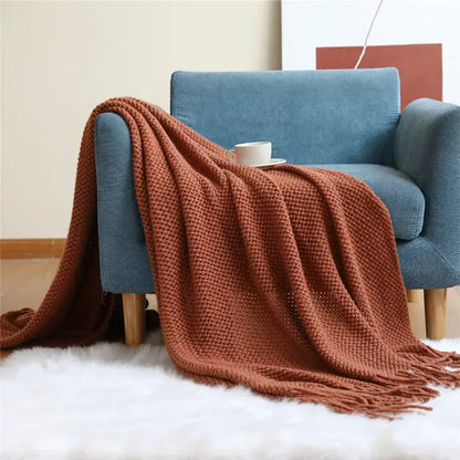 A rust-colored cozy nordic knit textured tassel throw blanket draped over a blue armchair for nordic knit sofa decorbites cozy nordic