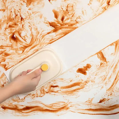 A beige scraper with yellow circular handle used for kitchen cleaning with cream and yellow silicone cleaning brush