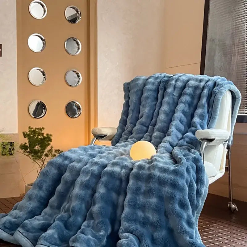 A plush light blue cozy bubble faux rabbit fur blanket draped over a white chair for bedroom decorbites cozy bubble decor