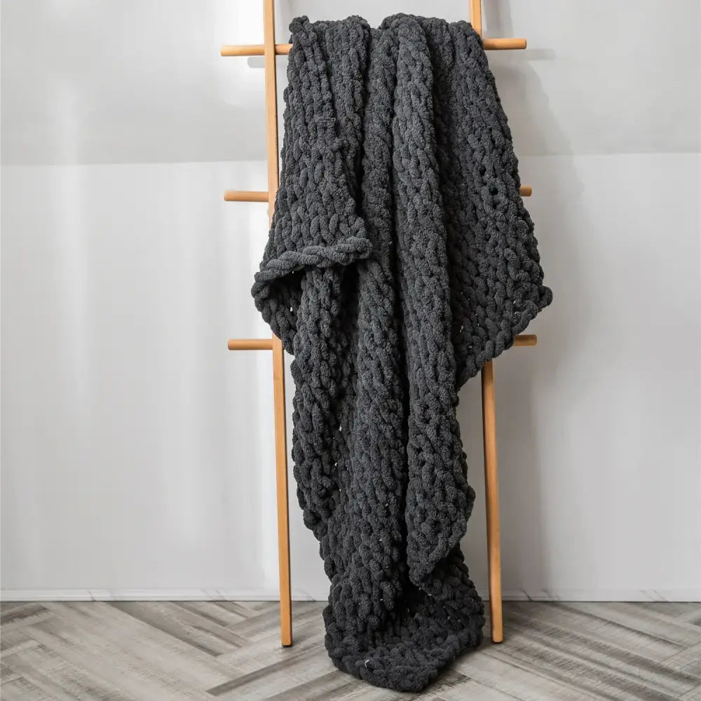 A thick dark gray decorbites cozy chenille chunky knit blanket draped over a wooden ladder for bedroom decor