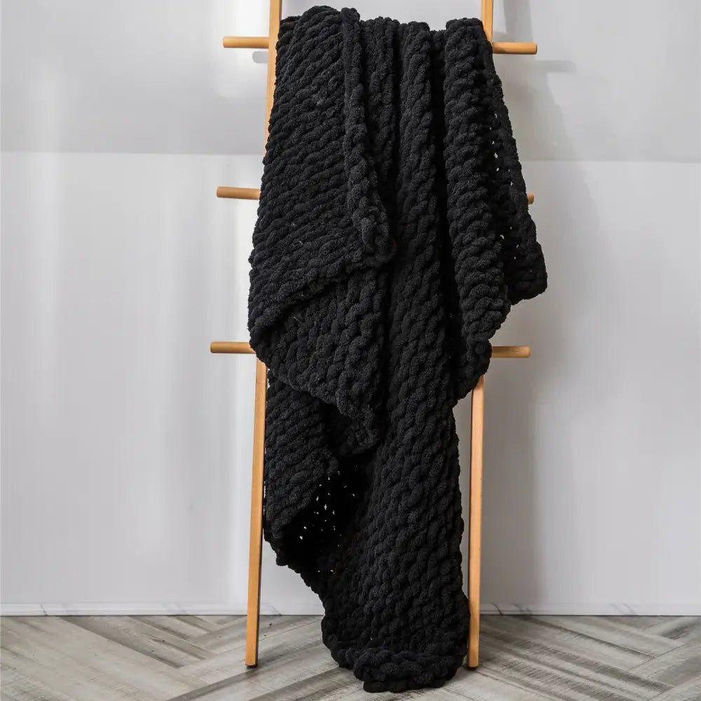 A thick black chenille chunky knit blanket draped over a wooden ladder for cozy chenille chunky decorbites decor