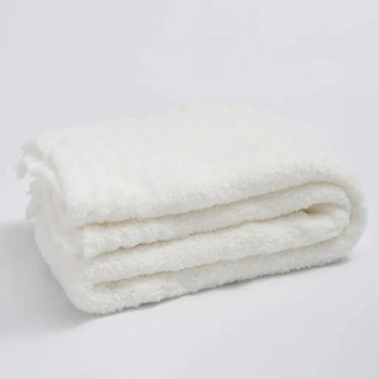 A plush white knitted throw blanket with a soft textured surface and ribbed microfiber edges for bedroom use