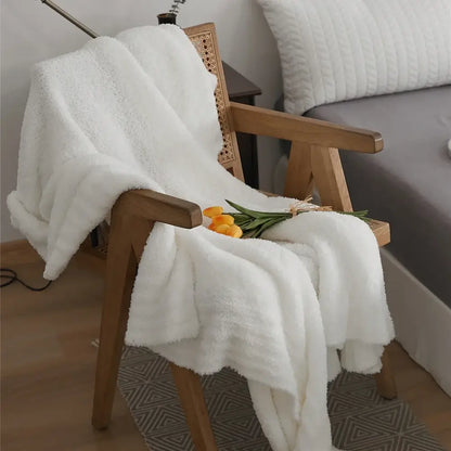 A cream knitted throw blanket in plush microfiber fleece draped over a wooden chair for bedroom use