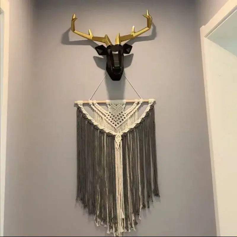 A modern geometric deer head wall hanging with gold antlers and black face above a cream and lavender cotton macrame decorbites living room tapestry