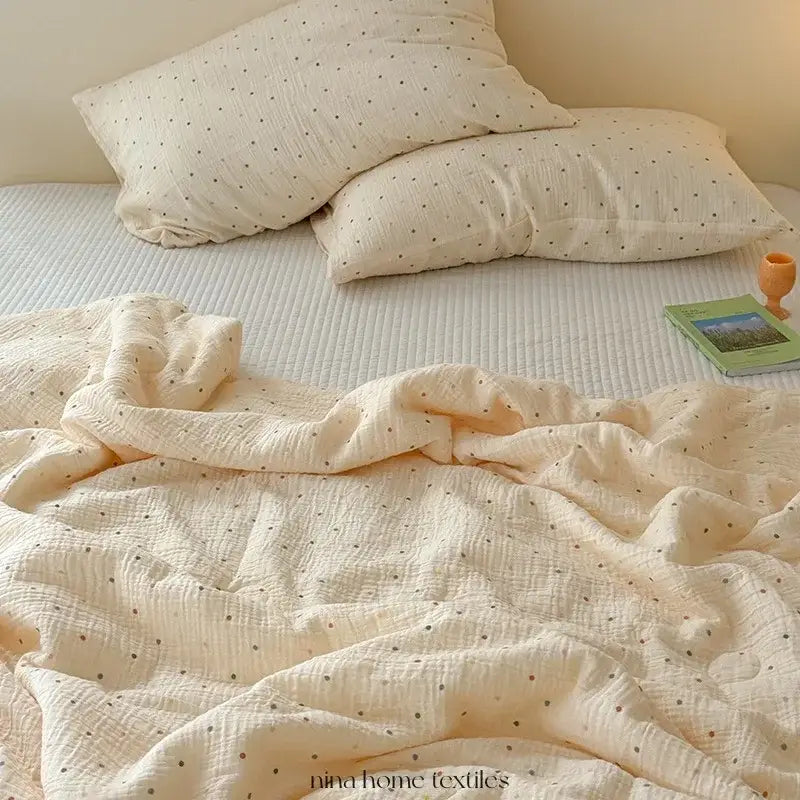 Cream polka dot floral quilt set with a cream-colored muslin quilt featuring subtle black polka dots draped on bed
