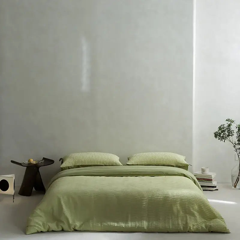 A soft sage green ribbed duvet bedding set made of cotton foam yarn with matching pillows on a minimalist bed
