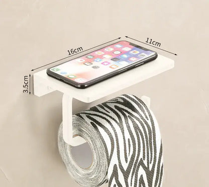 White plastic toilet paper holder with integrated phone shelf holding black smartphone in cream white bathroom set with towel rack