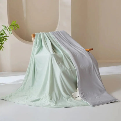 A creamy white and mint green ice cream silk quilt with a smooth satin finish draped over a wooden chair by decorbites