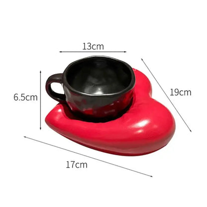 A creative heart porcelain coffee mug set featuring a glossy red ceramic heart saucer with a black glazed cup nestled inside