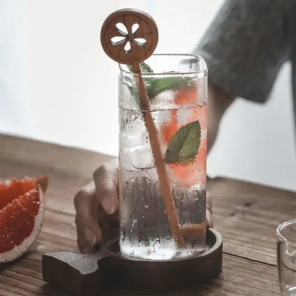 A clear decorbites creative square glass with gold rim filled with pink drink ice mint and wooden citrus stirrer