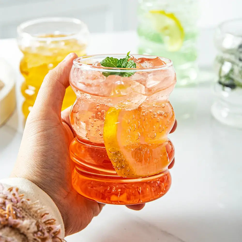 A clear textured glass creative styling glass tumbler with segmented design holds orange beverage with lemon and mint garnish
