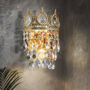 Gold-toned crown shaped wall mounted lighting with clear crystal prisms in aged brass for bedroom decor