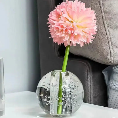A clear textured crystal bubble ball vase with internal bubbles holding a single pink artificial flower for decorbites decor