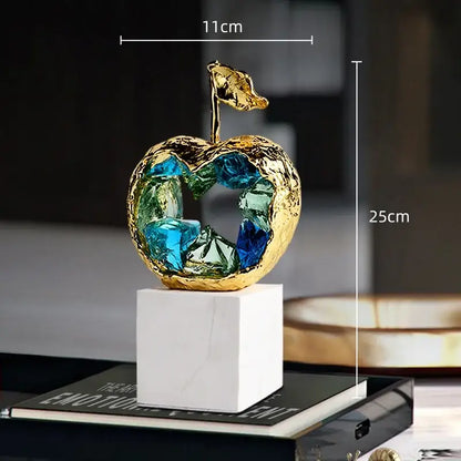 A golden decorbites crystal fruit sculpture with blue and green glass crystals on a white marble base for living room decor