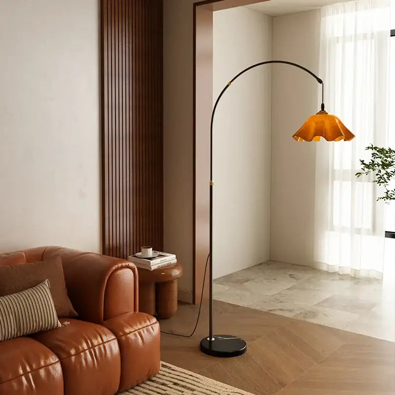 A sleek black curved floor lamp with an amber petal glass shade beside a living room shelf