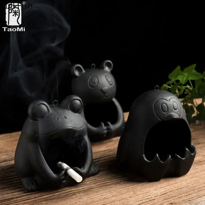 Cute black and gold ceramic ashtray shaped like a cartoon animal frog holding a cigarette with rising smoke for decor