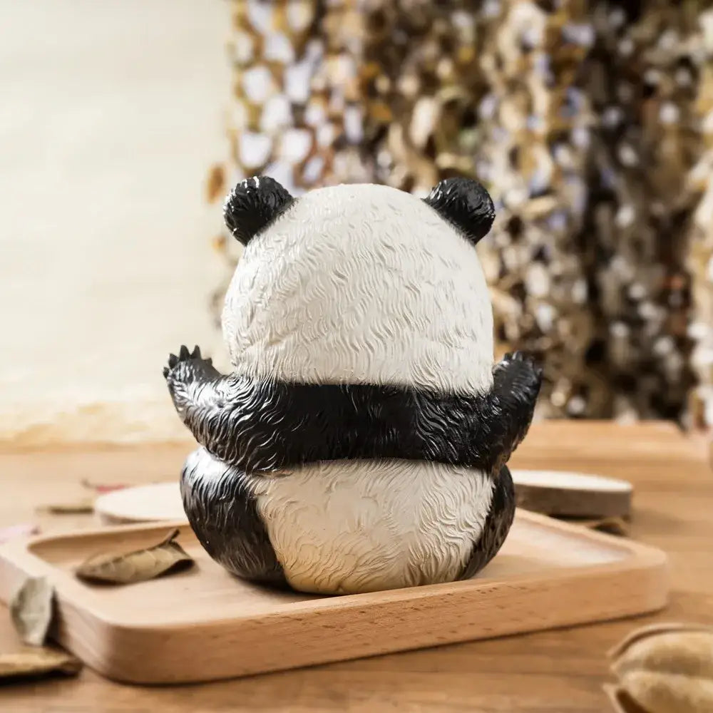 A black and white panda baby figurine with textured fur sitting on a wooden tray for living room decor