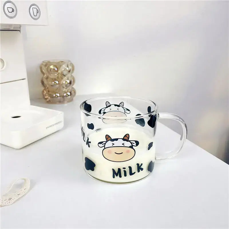 Clear glass mug with black cow pattern and smiling cartoon cow face featuring milk text with spoon lid for dining room use